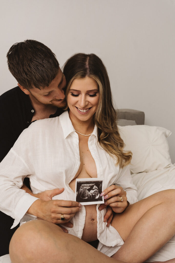 Séance maternité lifestyle à domicile, future maman et partenaire dans un décor minimaliste et lumineux, photo professionnelle réalisée par une photographe lifestyle au Québec.