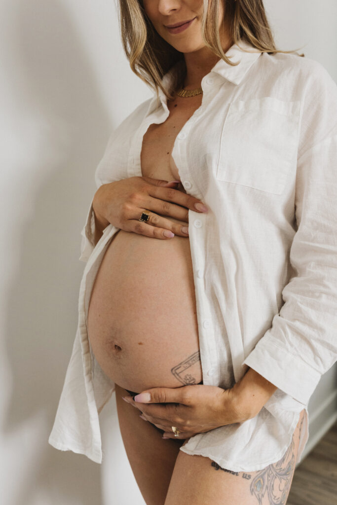 Gros plan du ventre d’une femme enceinte en séance photo maternité lifestyle, lumière douce et esthétique naturelle réalisée par une photographe lifestyle au Québec.