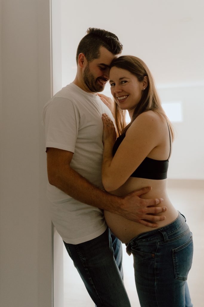 Couple attendant un bébé lors d’une séance maternité lifestyle intérieure, moment complice et naturel capté en lumière douce, photo professionnelle réalisée par une photographe maternité au Québec.