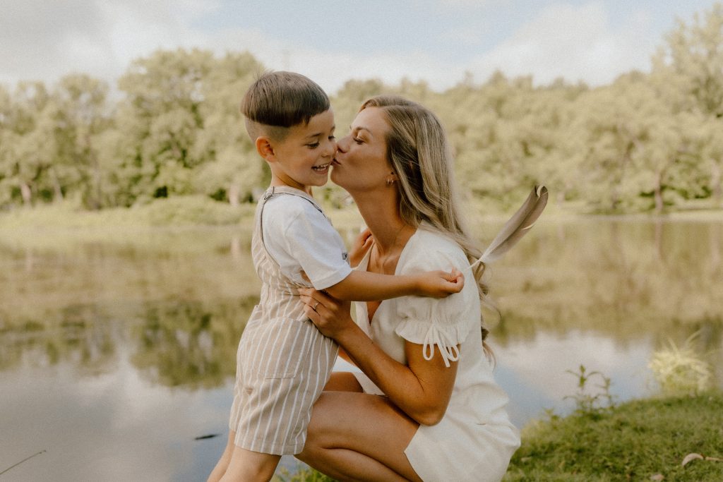 Maman embrassant son enfant lors d’une séance photo lifestyle familiale en nature, ambiance chaleureuse et naturelle photographiée par une photographe lifestyle à Contrecœur.