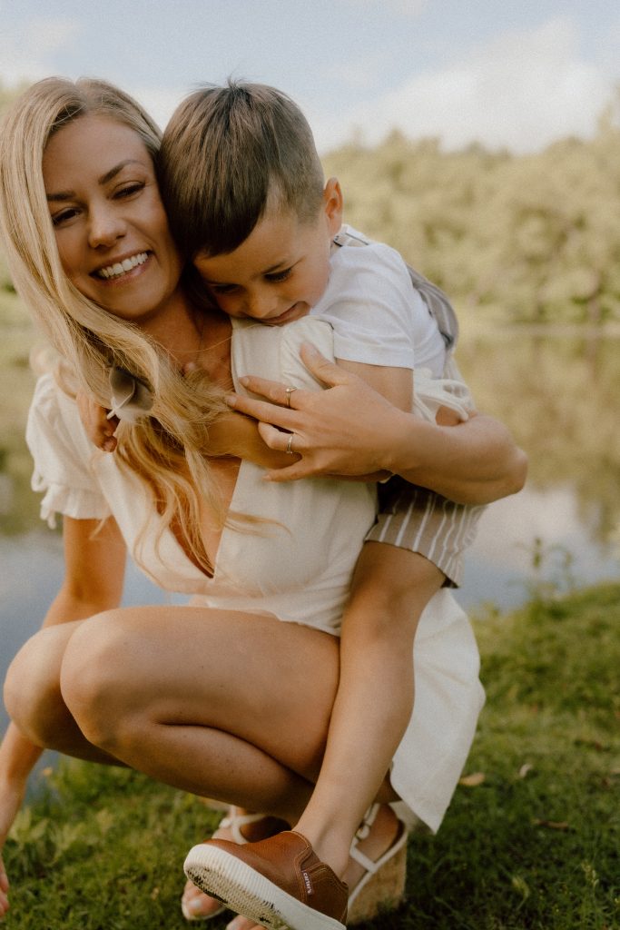 Maman tenant son jeune enfant dans ses bras au bord de l’eau, moment tendre et spontané capté en lumière naturelle par une photographe lifestyle spécialisée en photographie familiale au Québec.