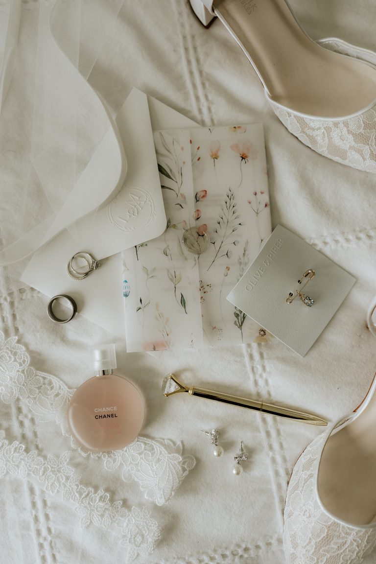 Détails des accessoires de la mariée comprenant des chaussures en dentelle, un parfum Chanel, des bijoux et une lettre florale.