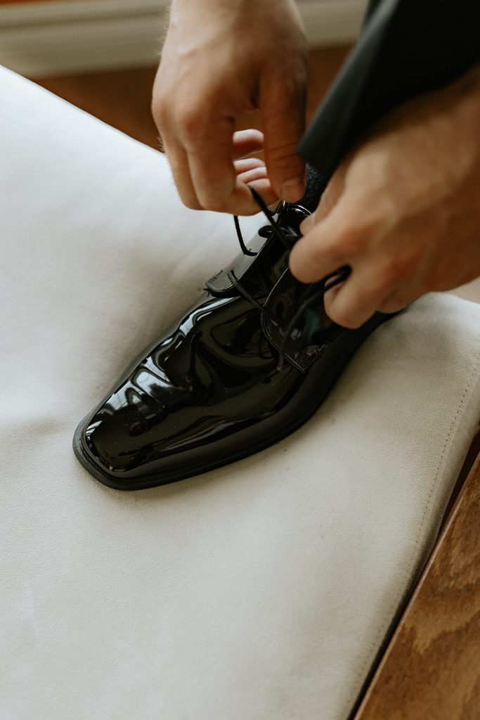Photo de proche du marié qui attache son soulier lors des préparatifs de son mariage.