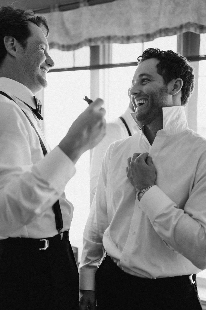 Photo en noir & blanc de deux garçons d'honneur s'aidant à se préparer avant le mariage.