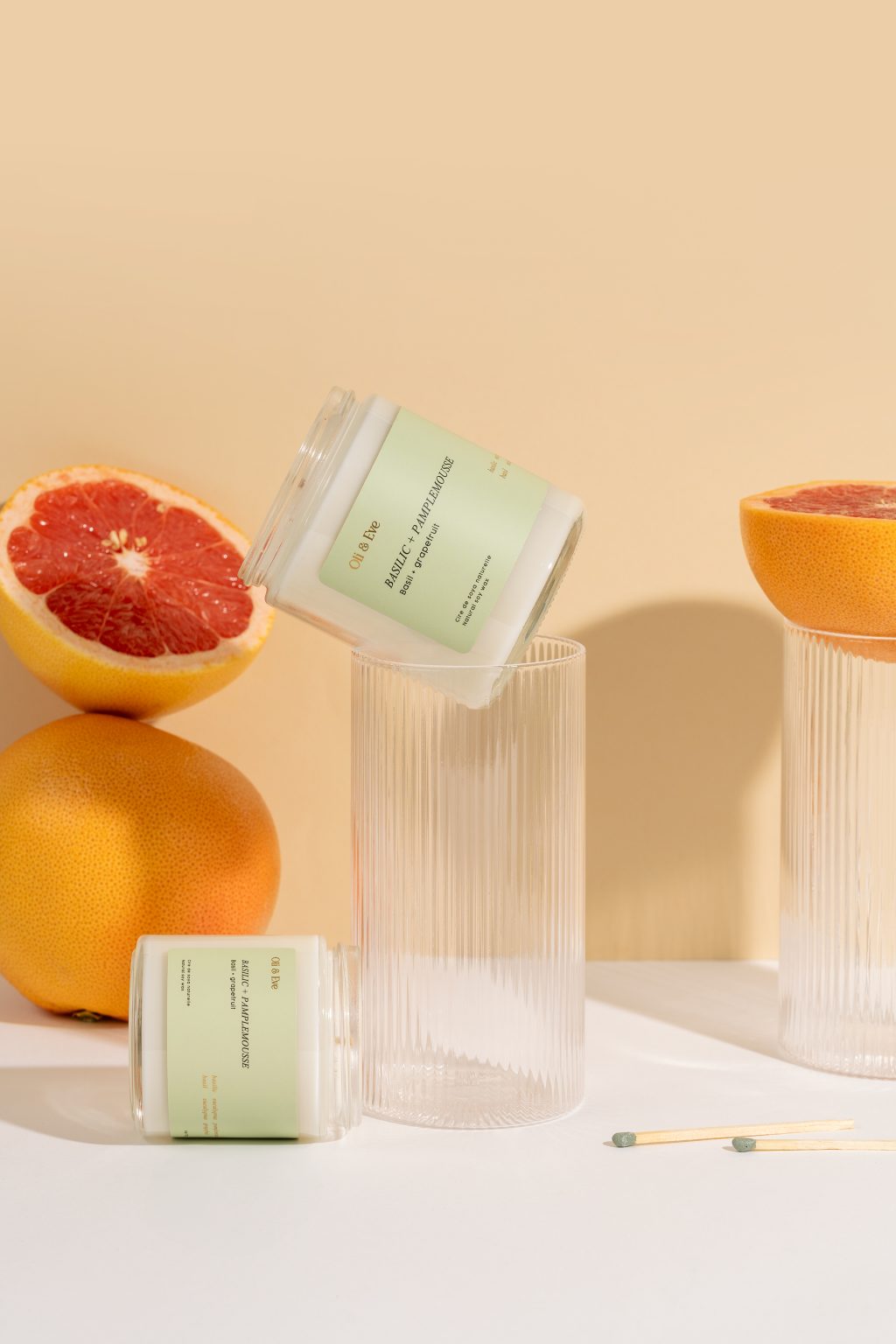 Photographie de bougies avec pamplemousses et verres en relief sur fond beige – composition créative et vitaminée pour marque bien-être