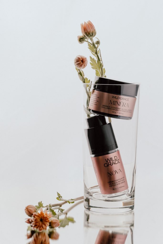 Photographie professionnelle de produits de soins Wild Grace disposés dans un verre avec éléments floraux, esthétique épurée et lumière douce, photo produit beauté réalisée par une photographe commerciale au Québec.