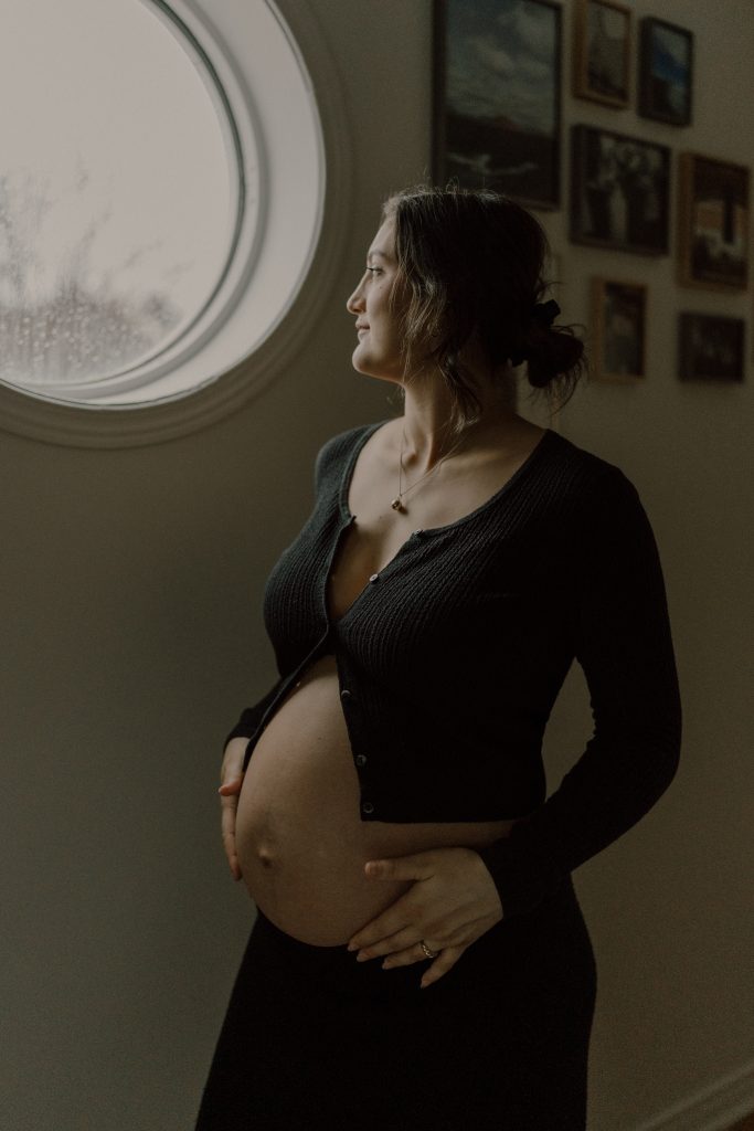 Portrait maternité doux et lumineux d’une femme enceinte près d’une fenêtre, lumière naturelle et ambiance intime, photo professionnelle réalisée par une photographe maternité au Québec.