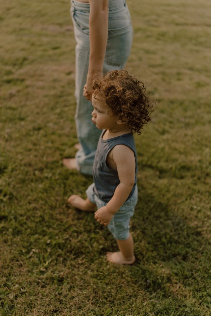 Jeune enfant marchant main dans la main avec un parent dans un champ, photographie lifestyle familiale naturelle réalisée par une photographe au Québec.