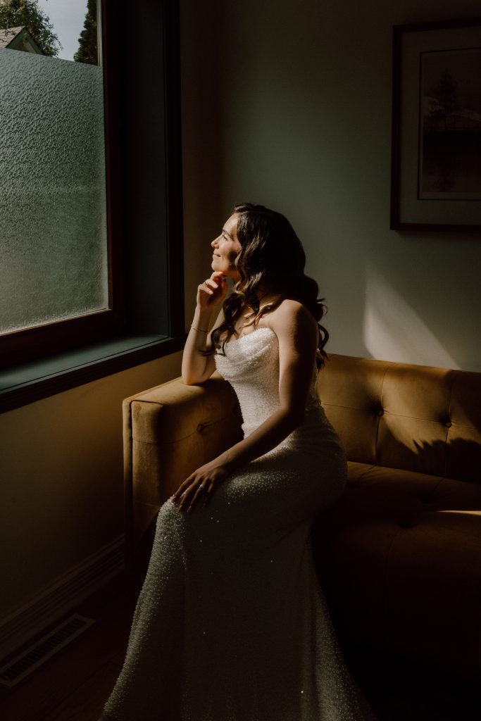 Portrait de la mariée assise près d’une fenêtre, baignée de lumière naturelle et d’ombres douces, ambiance élégante et intime, photo de mariage réalisée par une photographe professionnelle au Québec.