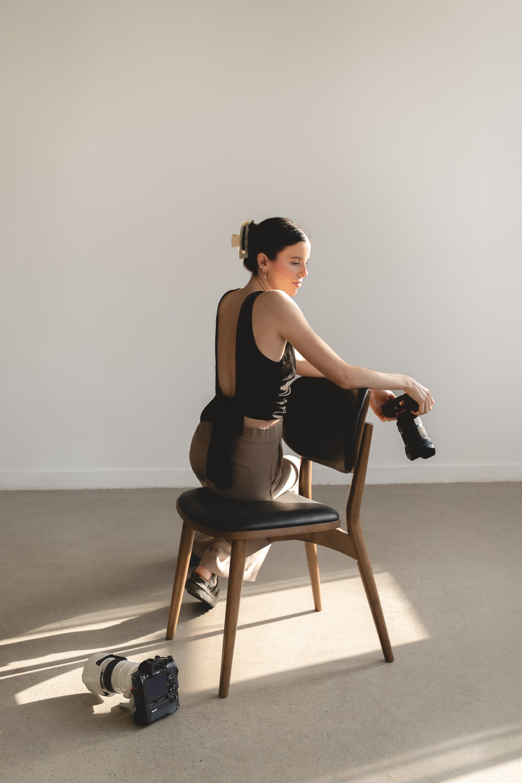Photo professionnelle réalisée par une photographe commerciale montrant une femme assise dans un studio lumineux, éclairée par une lumière naturelle douce, tenant un appareil photo; ambiance minimaliste et contemporaine. (photographe commerciale Québec, branding, portraits corporatifs, Montréal)