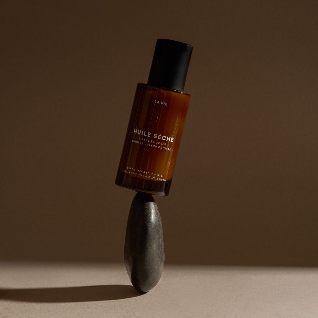 Flacon d’huile sèche Atelier La Vie Apothicaire délicatement posé sur une pierre sombre dans une mise en scène épurée aux tons chauds. Photographie de produit professionnelle mettant en valeur l’élégance, la simplicité et le caractère naturel du soin.