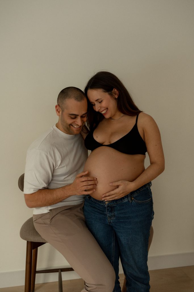 Couple attendant un bébé partageant un moment tendre, les mains posées sur le ventre arrondi de la future maman dans un décor lumineux et naturel. Photo professionnelle réalisée par une photographe spécialisée en maternité à Montréal, idéale pour immortaliser les liens familiaux avant l’arrivée de bébé.