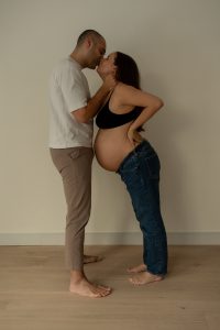 Future maman et son partenaire échangent un baiser dans un studio minimaliste aux tons neutres, créant une scène remplie de douceur et de complicité. Photo professionnelle réalisée par une photographe de grossesse au Québec, mettant en valeur l’amour et l’anticipation de cette étape de vie.