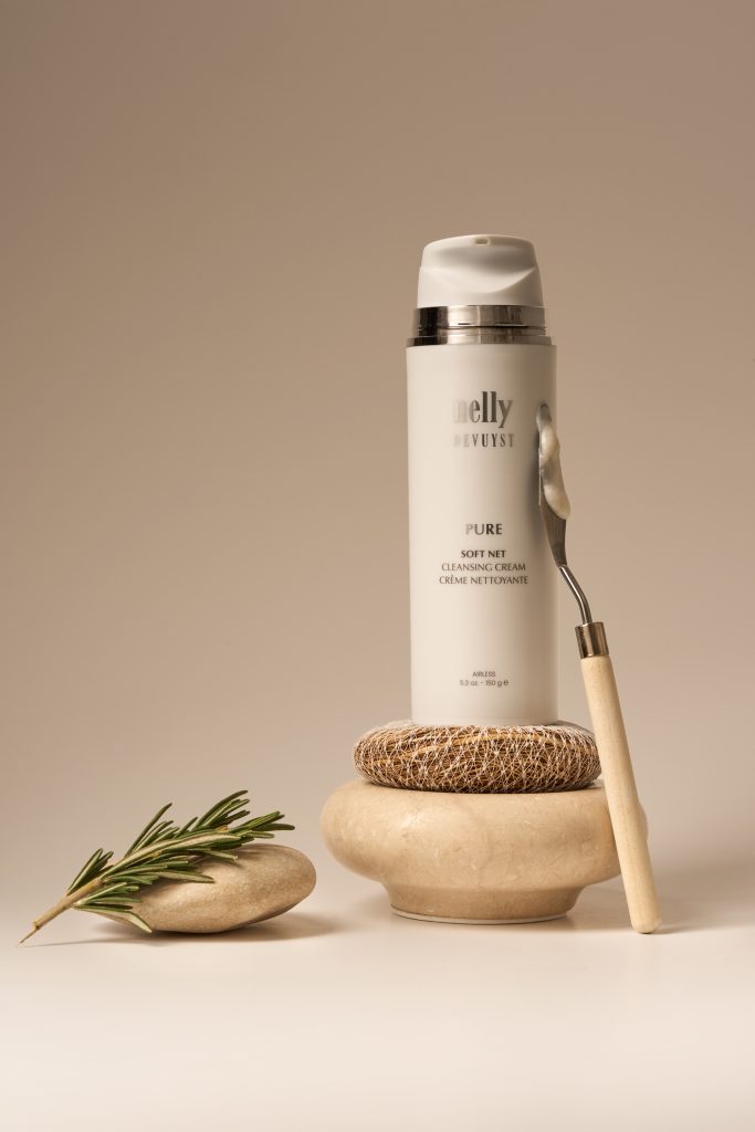 Flacon de gel nettoyant Pure de Nelly De Vuyst présenté dans une composition épurée avec pierres naturelles et branche de romarin sur fond beige. Photographie commerciale de produit beauté mettant en valeur l’identité naturelle et raffinée de la marque.