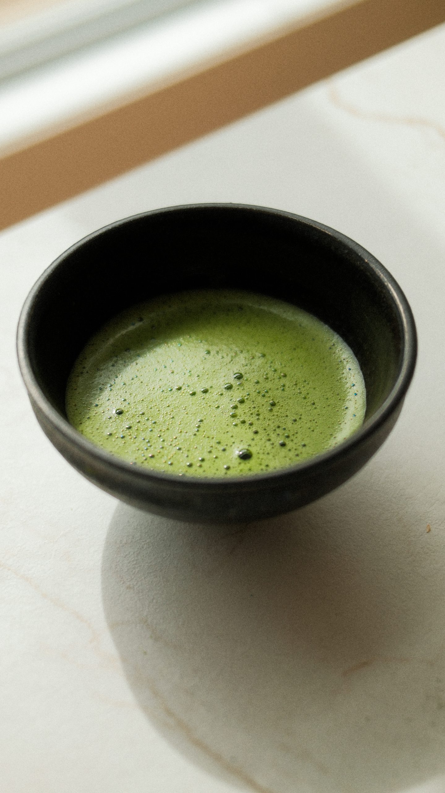 Bol de matcha mousseux présenté près d’une fenêtre dans une ambiance minimaliste et lumineuse aux tons naturels. Photo professionnelle réalisée pour une marque de thé, idéale pour illustrer un rituel bien-être et un mode de vie slow living.