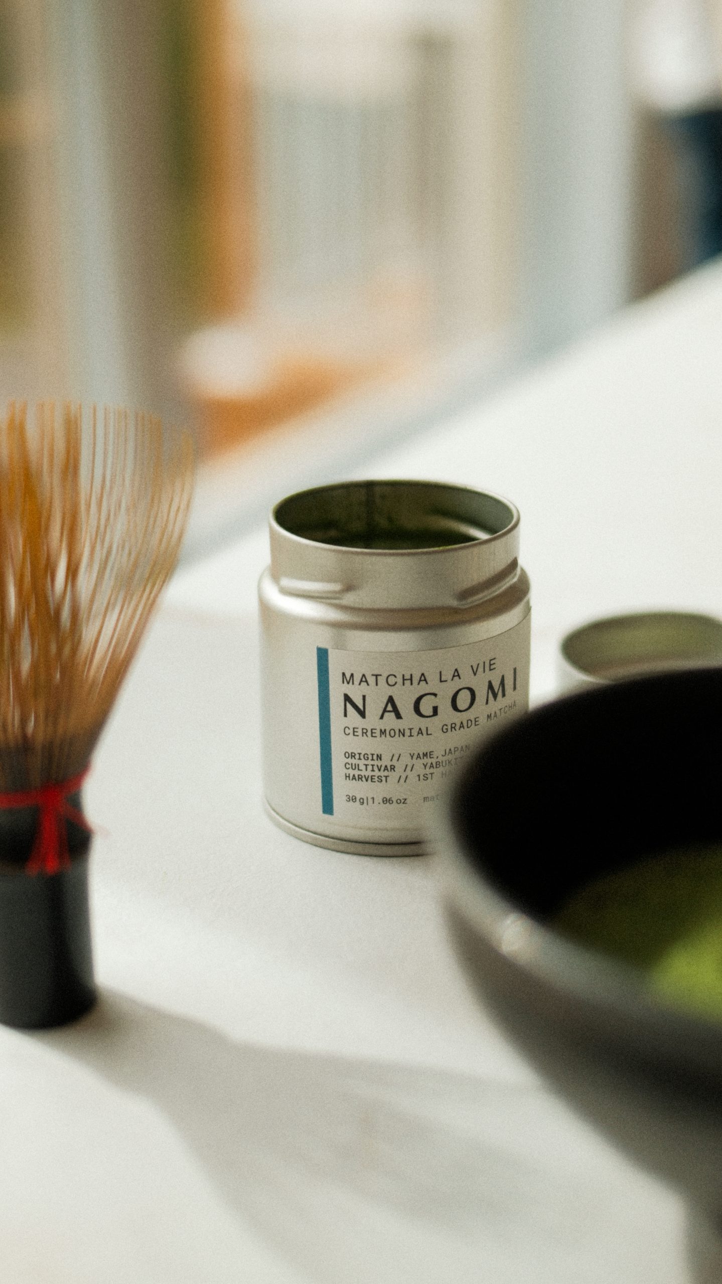 Boîte de matcha Nagomi de Matcha La Vie accompagnée d’un fouet traditionnel japonais et d’un bol de préparation, photographiés dans une lumière naturelle douce. Photographie de produit professionnelle réalisée pour une marque de thé, mettant en valeur l’univers du matcha cérémonial et le rituel de préparation.
