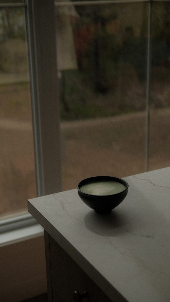 Bol de matcha posé sur un comptoir près d’une grande fenêtre laissant entrer une lumière douce et feutrée. Photographie lifestyle professionnelle mettant en scène un moment de calme, de pleine conscience et de dégustation de thé matcha.
