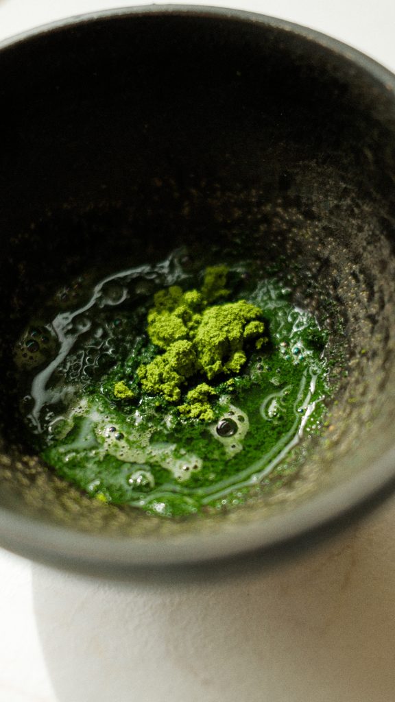 Gros plan d’un bol en céramique contenant du matcha fraîchement tamisé et mélangé à l’eau, révélant toute la richesse de sa couleur verte. Photographie culinaire professionnelle mettant en valeur la texture et la qualité du thé matcha cérémonial.