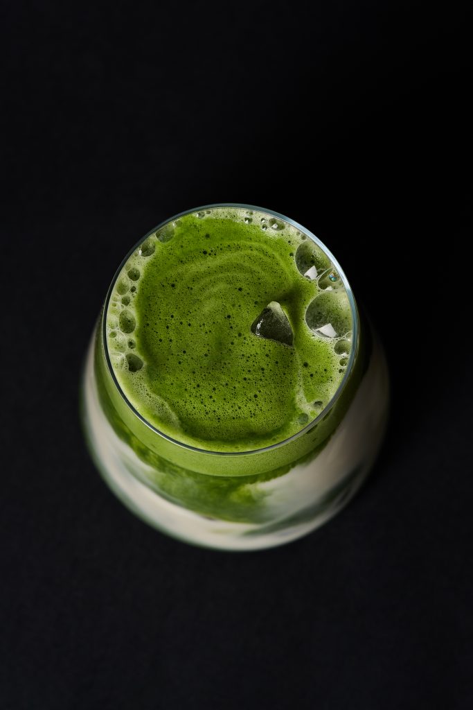 Verre de matcha glacé à la mousse verte onctueuse photographié sur un fond sombre créant un contraste élégant et moderne. Photographie de produit professionnelle réalisée pour Maison Minori, mettant en valeur la fraîcheur, la texture et l’intensité du thé matcha.