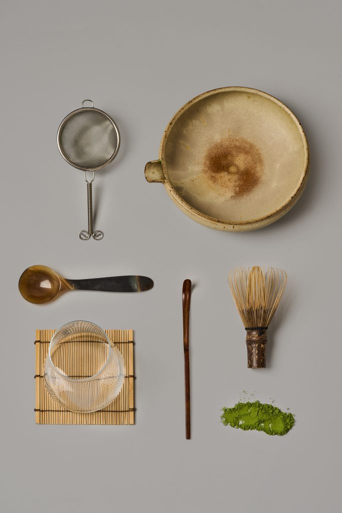 Vue à plat d’un ensemble d’accessoires de préparation du matcha comprenant bol, fouet en bambou, tamis, cuillère et poudre de thé sur fond clair minimaliste. Photo professionnelle réalisée pour Maison Minori, parfaite pour le commerce électronique et le contenu éducatif autour du matcha.