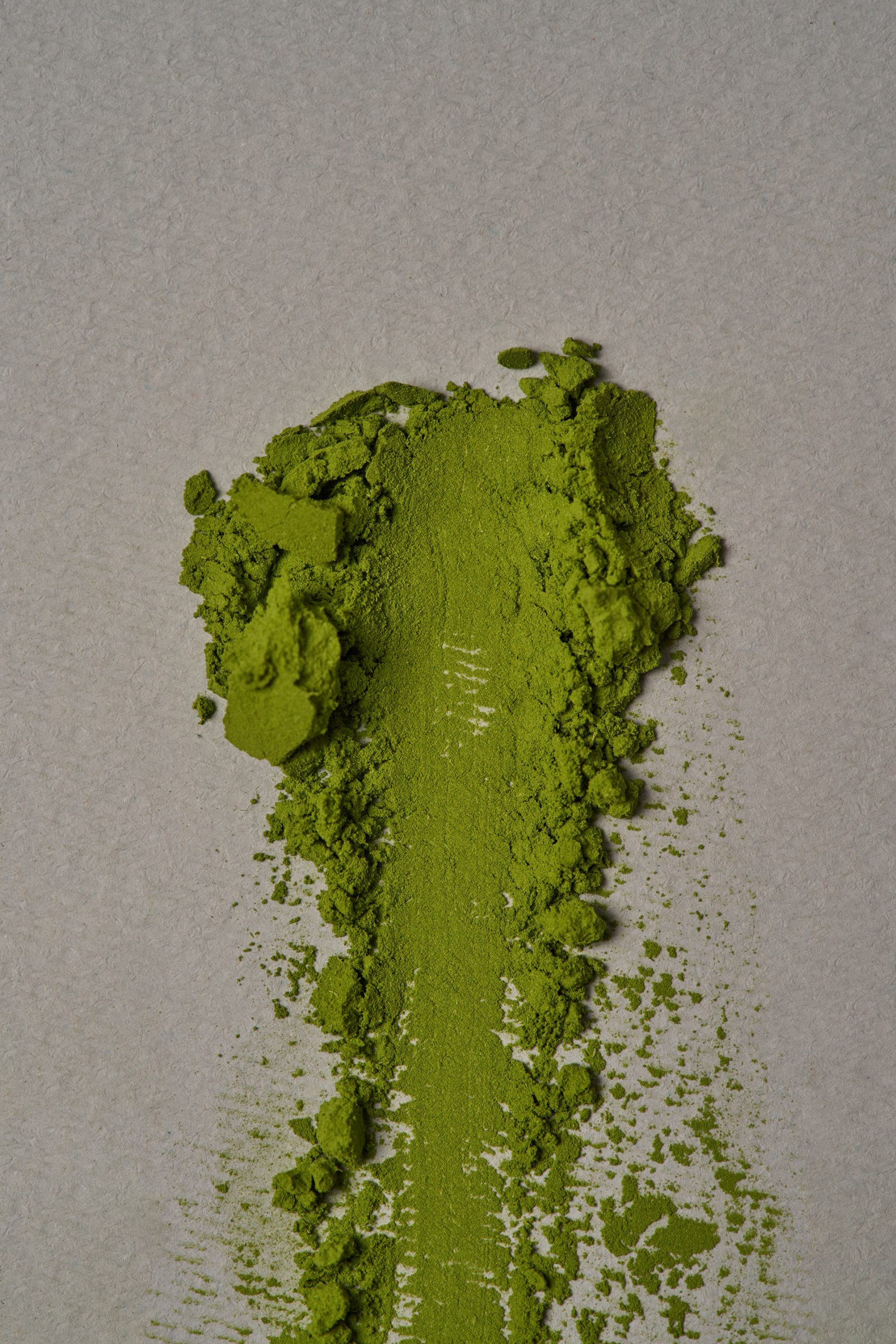 Poudre de matcha vert vif étalée sur une surface neutre, révélant sa texture fine et sa couleur éclatante. Photo professionnelle de produit réalisée pour Maison Minori, idéale pour illustrer la qualité et l’authenticité du thé matcha cérémonial.