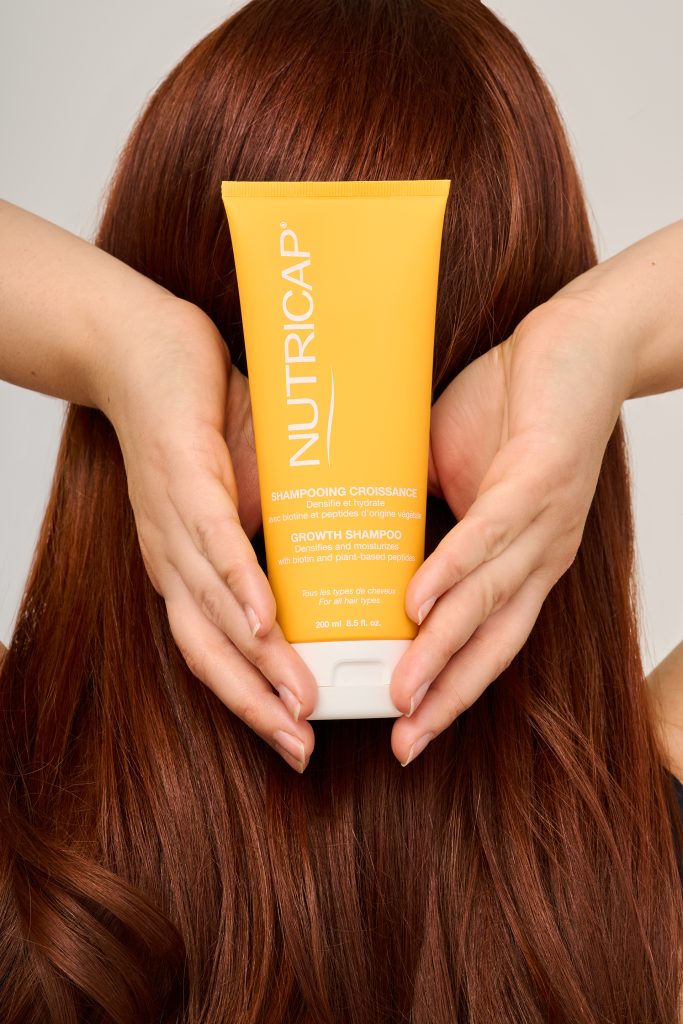 Tube Nutricap tenu devant une longue chevelure rousse brillante, illustrant les soins destinés à la croissance et à la santé des cheveux. Photo professionnelle réalisée pour une marque de beauté, mettant l’accent sur les résultats et la qualité des produits capillaires.