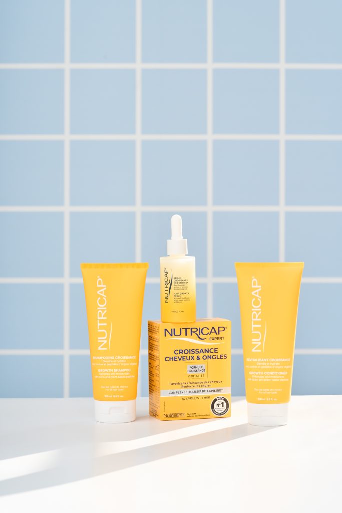 Collection de produits Nutricap soigneusement disposés sur une surface blanche devant un fond bleu pastel inspiré de l’univers du bien-être. Photo professionnelle de produit réalisée pour le commerce électronique, la publicité et la création de contenu beauté.