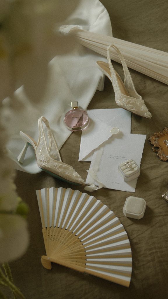 Photo des détails d’un mariage avec papeterie, chaussures, bague et éventail, capturés dans une esthétique naturelle et élégante.