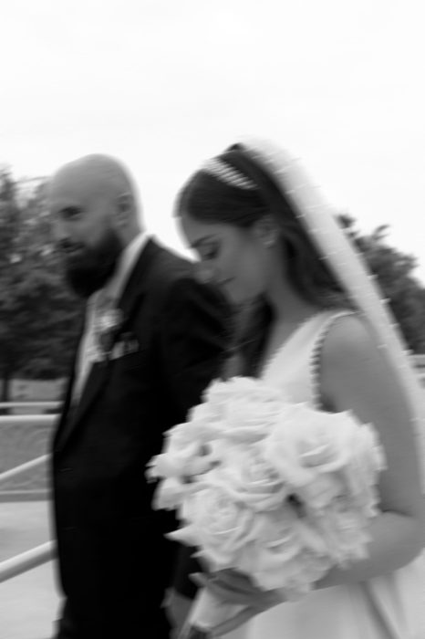 Couple de mariés marchant côte à côte en noir et blanc, la mariée tenant son bouquet et portant un voile, photo de mariage naturelle captée par une photographe de mariage au Québec.