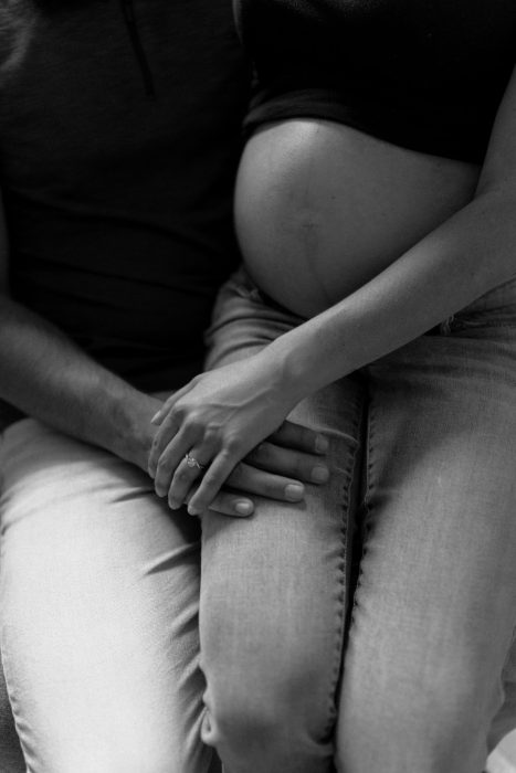 Gros plan en noir et blanc d'un couple tenant tendrement le ventre de la future maman, symbolisant l'attente de leur enfant.