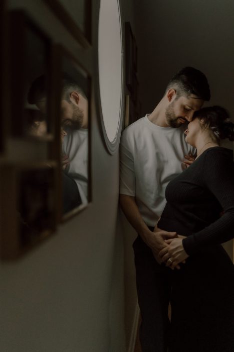 Couple en séance maternité lifestyle à domicile, moment intime et doux capté près d’un miroir en lumière naturelle, photo professionnelle réalisée par une photographe lifestyle spécialisée en maternité au Québec.