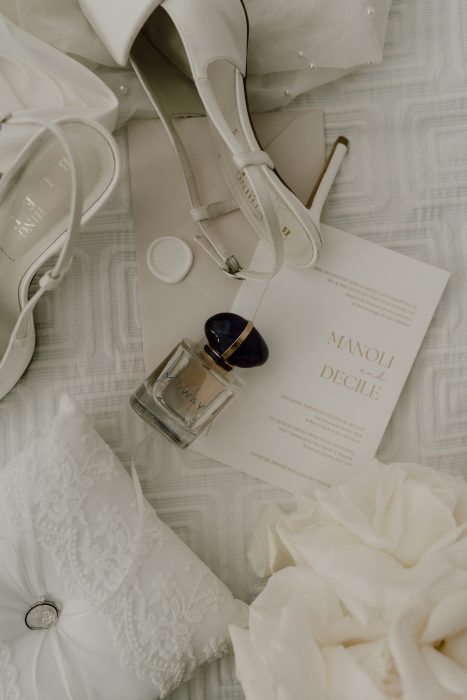 Détails de préparation de mariage avec chaussures de la mariée, parfum, papeterie et robe blanche dans une ambiance douce et lumineuse, photo de mariage réalisée par une photographe professionnelle au Québec.