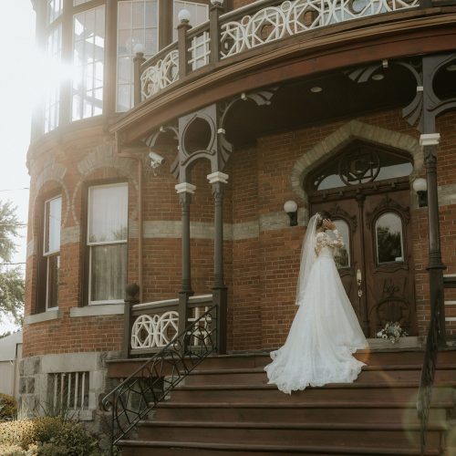 Mariée en robe blanche avec voile devant Le Château Saint-Antoine, baigné de lumière naturelle, photo de mariage élégante réalisée par une photographe professionnelle au Québec.